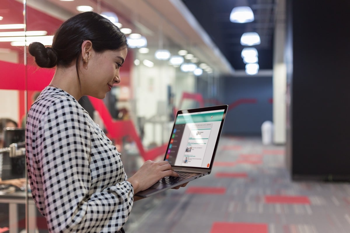 Standing woman creating an employee newsletter on a laptop